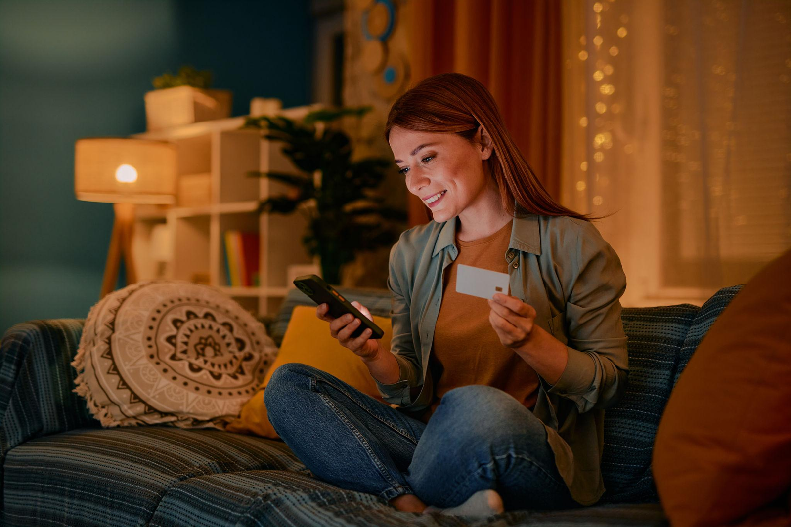 Mulher sentada no sofá analisando uma compra pelo celular